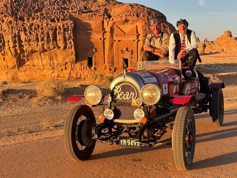 Matthew Benns (right), Editor-at-Large of Sydney’s The Daily Telegraph, and Warren Brown (left), an editorial cartoonist for the same outlet, pose inside a 1925 Bean model car near the ancient carved tombs of Hegra, the sister city of Petra, in Jordan.