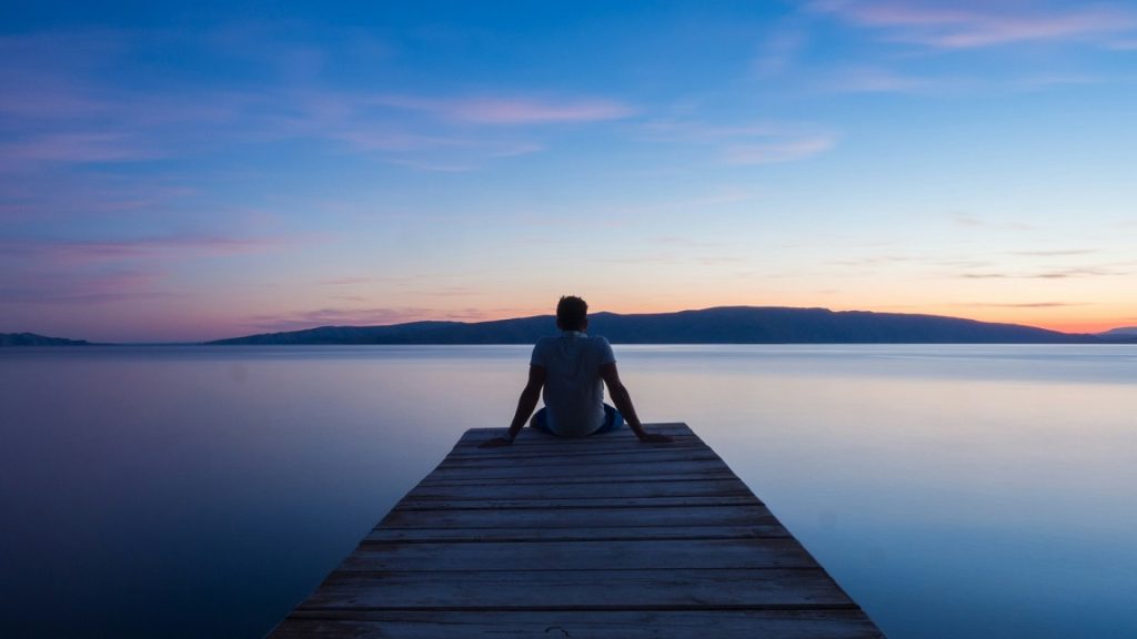 Man overlooking the sea while sitting on the edge of a pier.