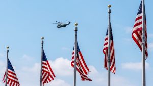 A helicopter flies past a row of US flags.