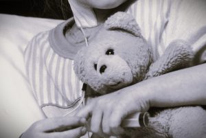 A young cancer patient hugs a teddy bear.
