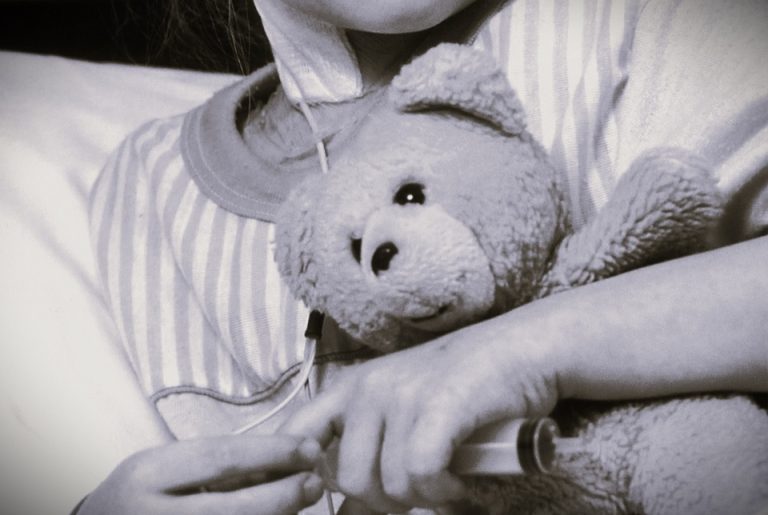 A young cancer patient hugs a teddy bear.