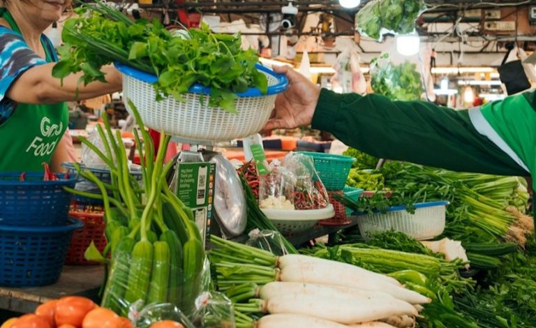 A customer passing a basket of vegetables to a stall owner in a wet market.