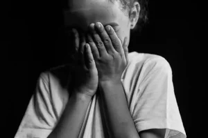 A child covers his face with the palms of his hands.