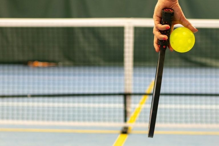 An image of a hand with a pickleball bat and a ball.