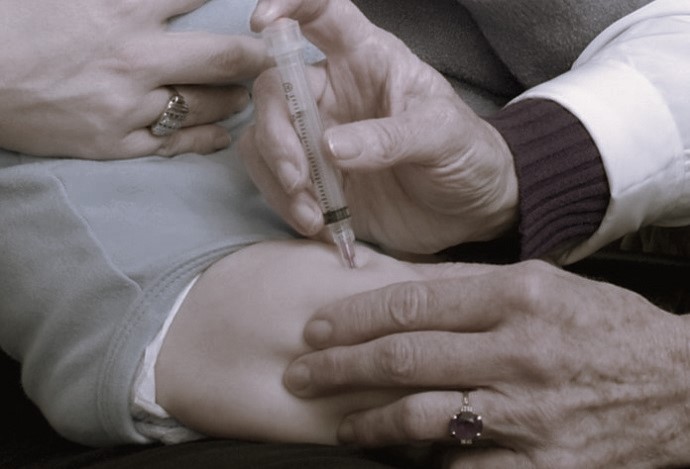 A doctor injects a baby's thigh with vaccine.