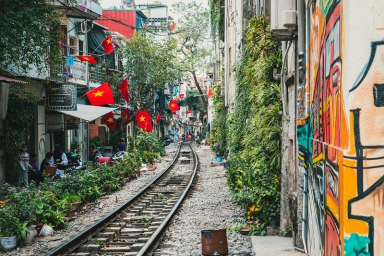 Cafes and shops line both sides of an active rail track in Hanoi with the Vietnam flags decorating the sides.