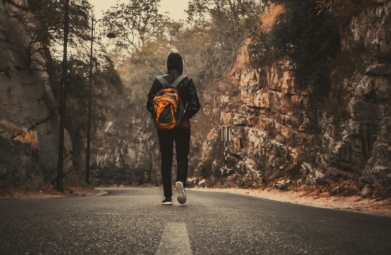 A man with a backpack walking away on the road.