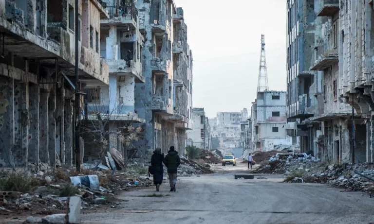 A couple walk past damaged buildings in Syria in 2022.